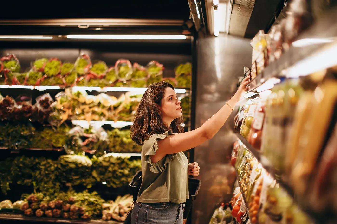 Woman shopping in grocery store produce section selecting packaged goods from shelf